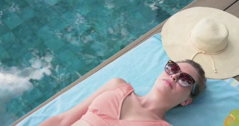 Sunlight sparkling on pool water causing woman reclining on towel lifting Stock Footage 344949317