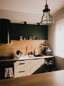 Sunlight streaming into modern kitchen featuring wooden furniture, vibrant green Stock Photos