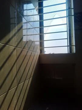 Sunlight streaming through barred window creating dramatic shadows on tiled wall Stock Photos