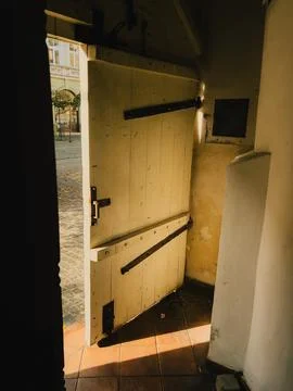 Sunlight streams into dark interior through an open, weathered wooden door Stock Photos
