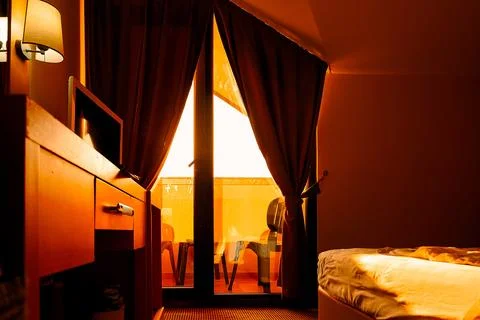 Sunlight streams into  room through brown curtains.  bed is visible, and smal Stock-Fotos