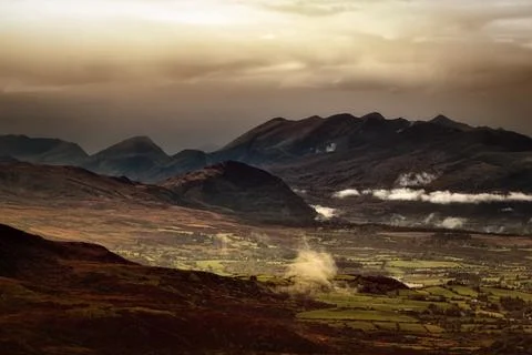Sunlight streams through dark clouds, illuminating parts of a valley 스톡 사진