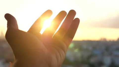 Sunlight streams through open hand against blurry cityscape at sunset cinem.. Stock-Footage 332471516