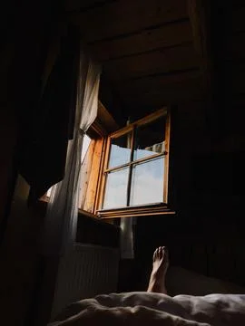 Sunlight streams through an open window in cozy wooden cabin, illuminating foot Stock-Fotos
