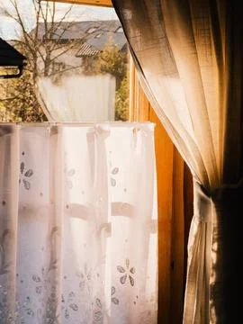 Sunlight streams through sheer white curtains with floral patterns, creating Stock-Fotos