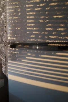 Sunlight streams through window blinds and a lace curtain Stock Photos
