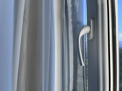 Sunlight streams through a window with a white curtain and a grey handle. The Stock Photos
