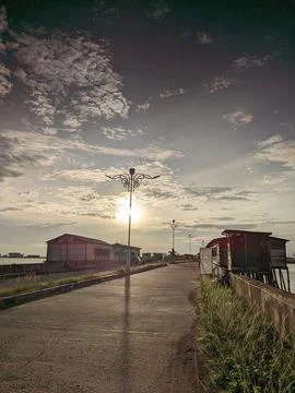 Sunlight through clouds illuminates buildings and lamps along coastal walkway 스톡 사진