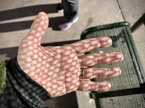 Sunlight through a textured grating creates pattern of dots and shadows on hand Stock Photos