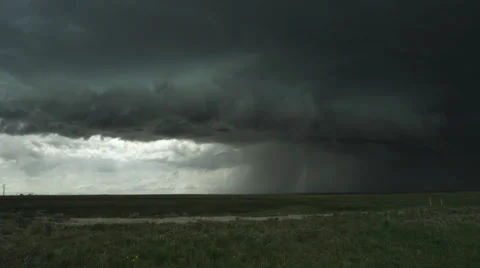 Sunlight under dark shelf cloud at left as heavy rain falls on prairie at right, Stock Footage
