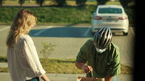 At sunlight young man courier in a safety helmet and medical mask delivering Stock Footage 138177900