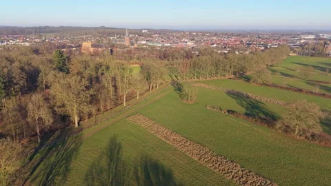 Sunlit aerial view of tree lined fields and winding paths leading to a town Видео 327041835