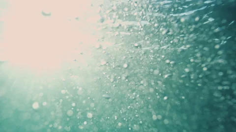 Sunlit Air Bubbles Drift Through Turquoise Water Beneath Illuminated Surface 動画素材 344032198