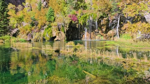 Sunlit autumn landscape featuring a calm lake, moss covered cliffs, and narrow Stock Footage 340866852
