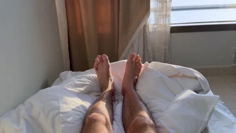 Sunlit Bare Legs Resting On White Bed Sheets Stock Footage 345475052