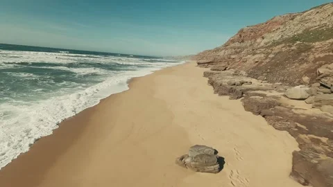 Sunlit beach meets rugged cliffs and crashing waves Video stock 341823234