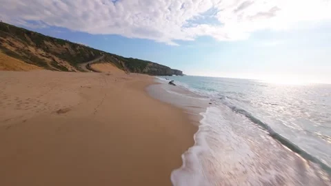 Sunlit beach scene with cliff backdrop and calm waves Stock Footage 340225583