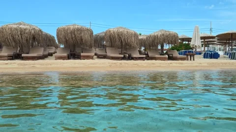 Sunlit beach with thatched umbrellas and lounge chairs. Trani Ammouda, Greece Stock Footage 339617842