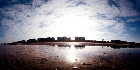 Sunlit Beachfront View with Reflections and Skyscraper Silhouettes Stock Photos