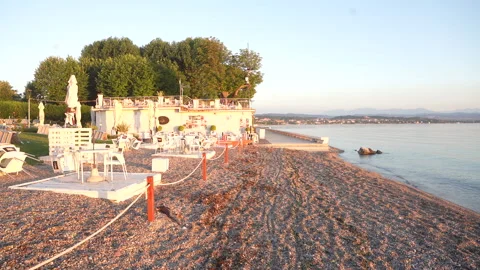 Sunlit beachside cafe with empty chairs and calm water view Stock Footage 287820569