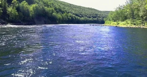 Sunlit blue river running between steep forested ridges Vidéo 71261572