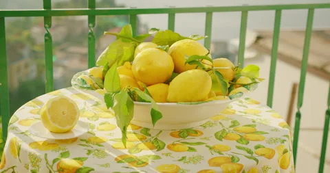 Sunlit bowl of fresh lemons on a patterned tablecloth, balcony setting. Fresh Stock Footage 273295675