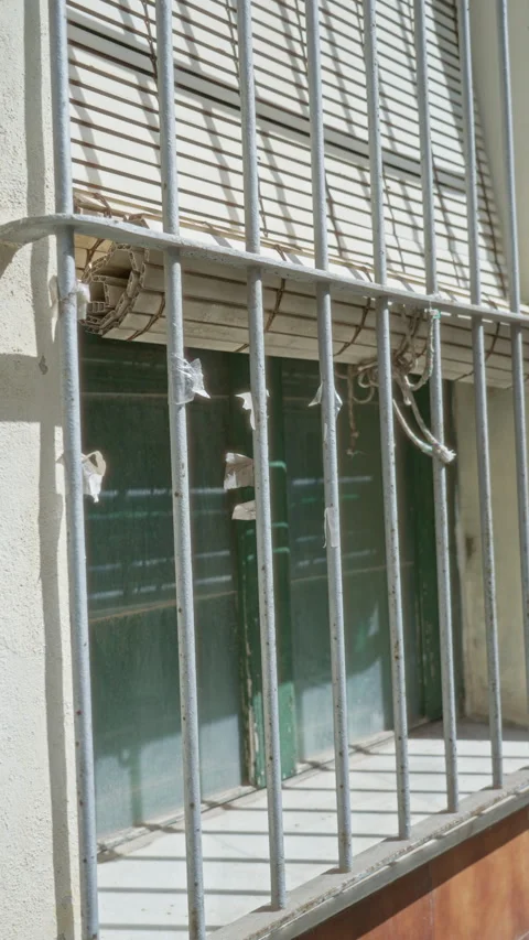 Sunlit building facade with barred windows casting shadows emphasizing secu.. Stock Footage 307373704