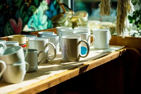 Sunlit Ceramic Coffee Cups Arranged on Wooden Cafe Counter Stock Photos