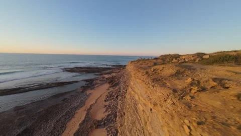 Sunlit cliff edge meets crashing sea at golden hour Stock Footage 344562911