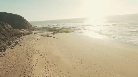 Sunlit cliffs meet gentle waves at golden shore Video stock 341826937