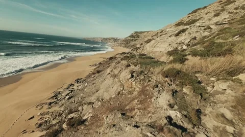 Sunlit cliffs meet golden sands beneath clear skies Video stock 341825734