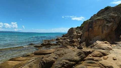 Sunlit cliffs meet turquoise sea, rocks line shore. Trani Ammouda, Greece Stock Footage 340638010
