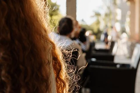 Sunlit close-up of long red curly hair at an outdoor cafe terrace Stock Photos