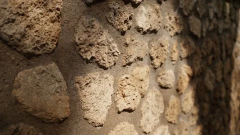 Sunlit close-up of Pompeii stone wall texture, revealing rough volcanic Stock Footage 335446909
