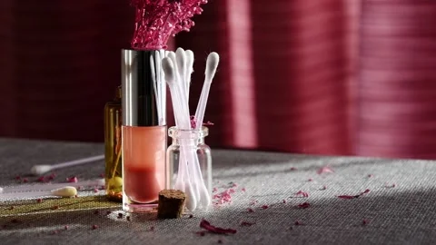 Sunlit cosmetic jars with lip gloss, cotton buds and falling lilac petals Stock Footage 149573032