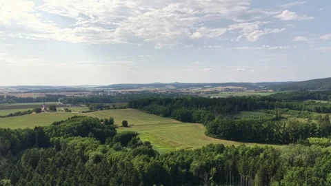Sunlit countryside rolling hills, patchwork fields, dense forests, distant Stock Footage 348504260