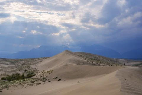 Sunlit desert dunes under a dramatic cloudy sky Stock Photos