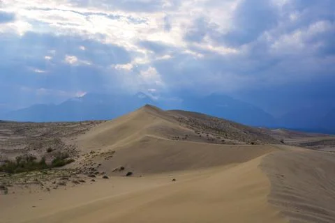 Sunlit desert dunes under a dramatic cloudy sky Stock Photos