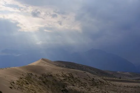Sunlit desert dunes under dramatic clouds and sunbeams Stock Photos