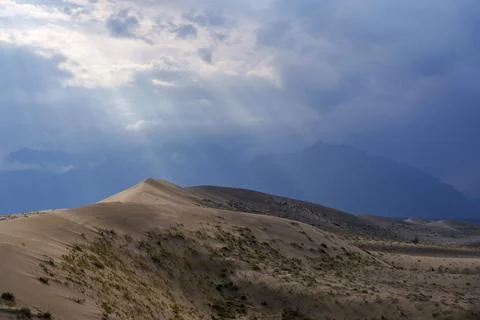 Sunlit desert dunes under dramatic clouds and sunbeams Stock Photos