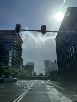 Sunlit empty city intersection with modern office towers, wet pavement, traffic Stock Photos