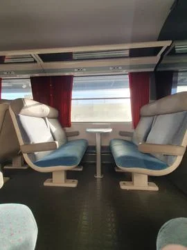 Sunlit empty train carriage featuring paired upholstered seats facing a small Stock Photos