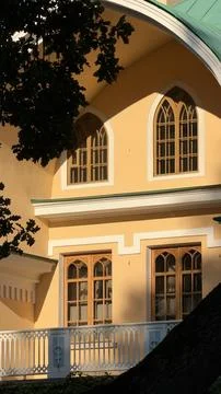 Sunlit facade of a yellow classic building featuring gothic-style arched wooden Stock Photos