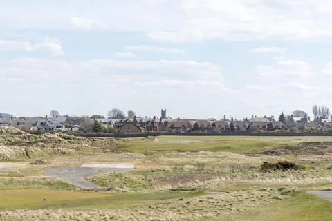 Sunlit field stretches toward distant Prestwick rooftops Stock Photos