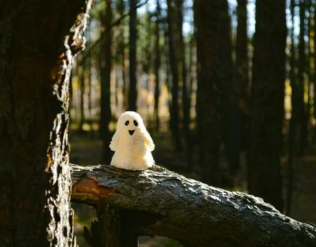 Sunlit ghost toy stands on a broken tree trunk in the forest Stock-Fotos