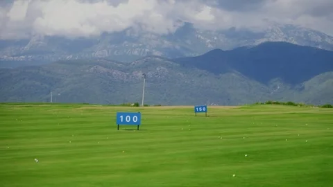 Sunlit golf driving range with 100 and 150 markers, mountains Vidéo 329413298