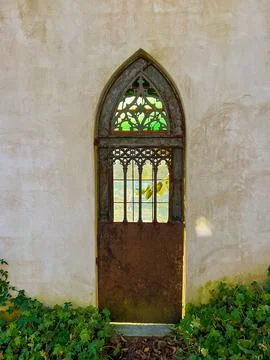 A sunlit gothic arch window door with stained glass in an old garden building Fotos de archivo