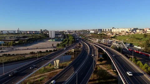 Sunlit highway bridges stretch over calm river with city skyline in background Stock Footage 345226379