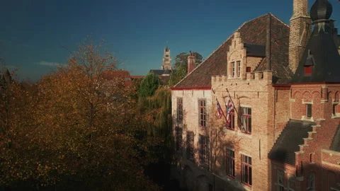 Sunlit historic brick building and autumn trees along Bruges canal Vídeo Stock 346674929