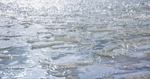 Sunlit ice shards drifting and glinting on dark rippling water, 8K Stock Footage 339239139